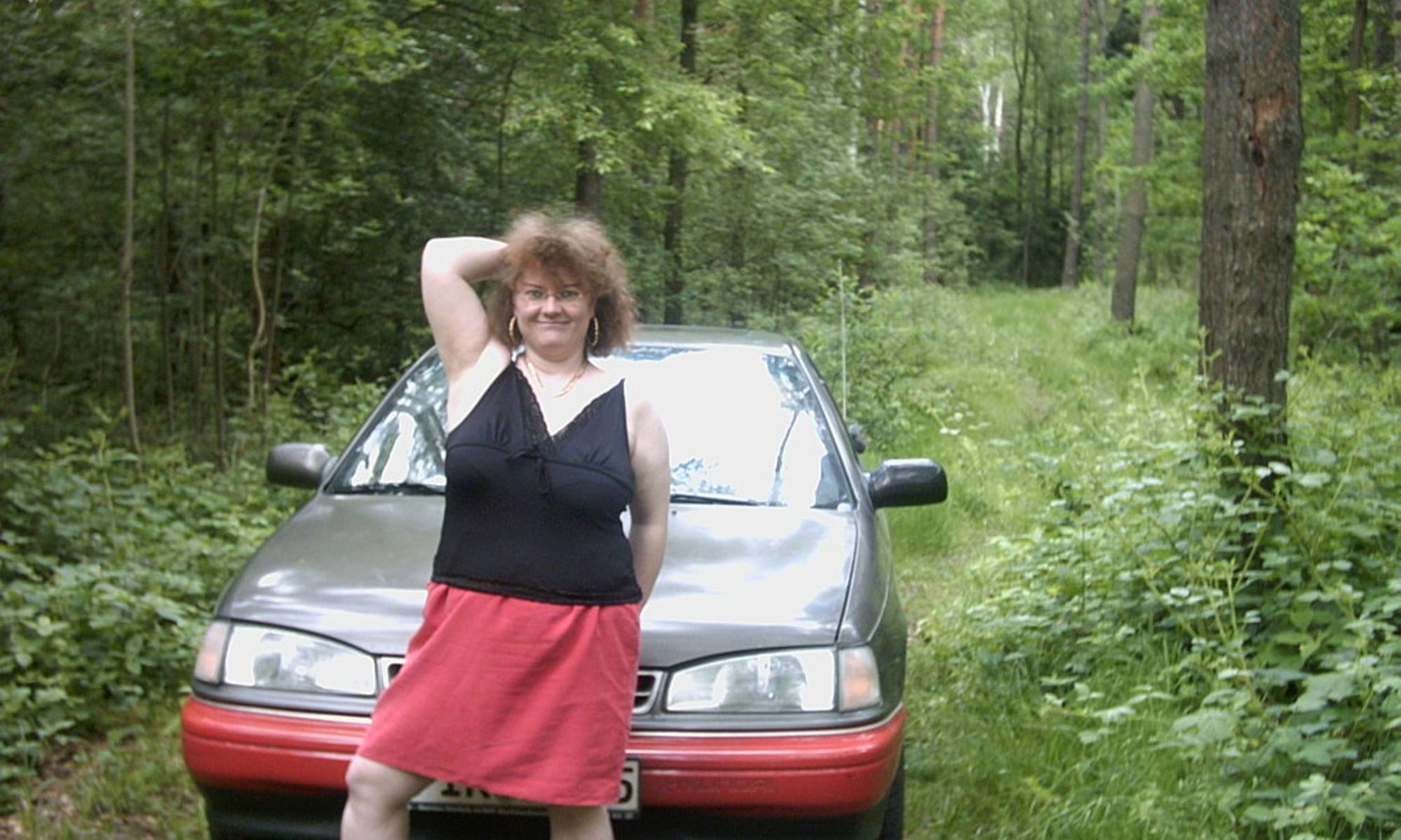 dicke Frau posiert vor ihrem Auto im Wald